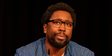 Dermot Daly presenting. wearing blue and white clothing, in front of a black background